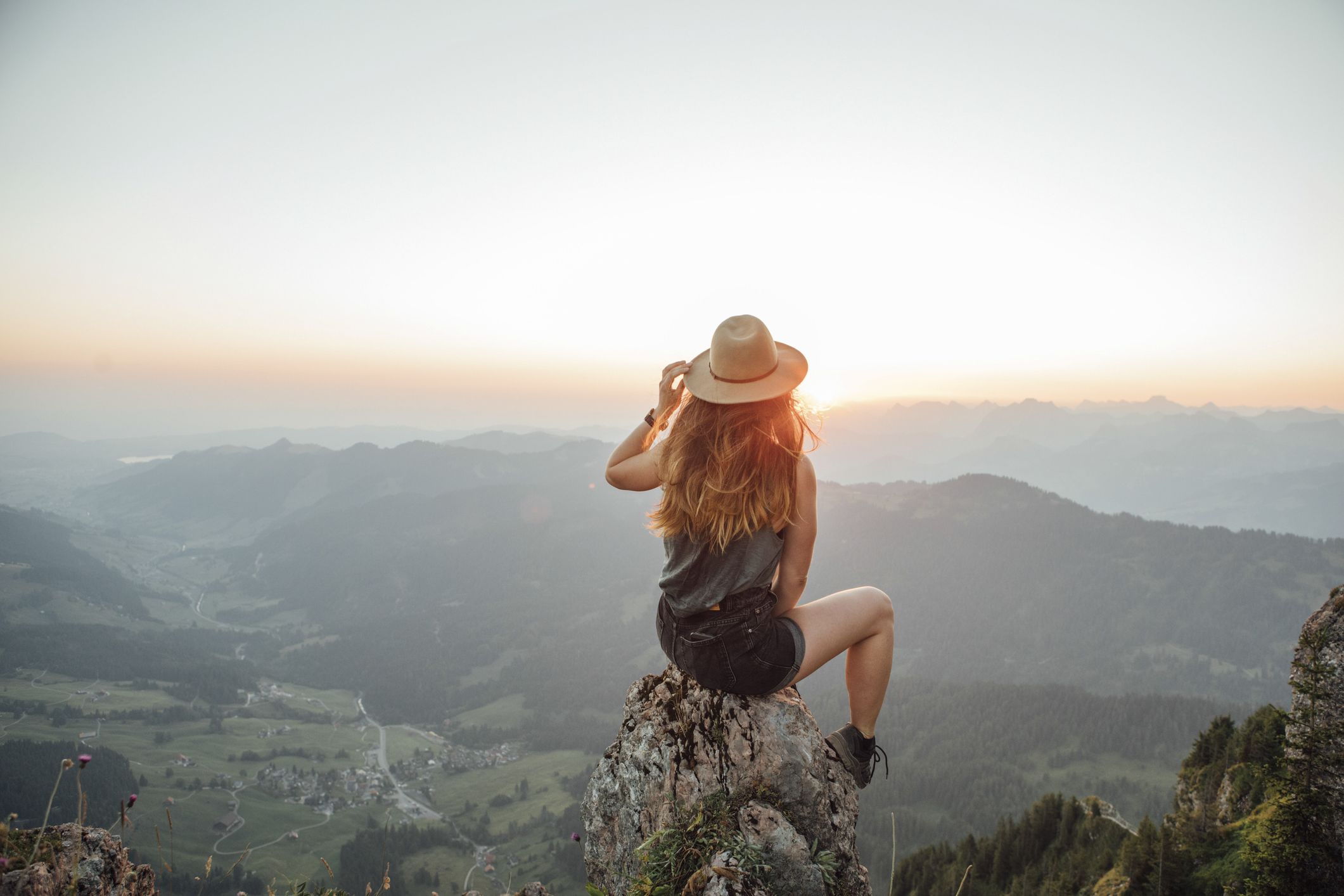 Une jeune femme est assise sur un rocher en montagne et contemple le panorama avec confiance.