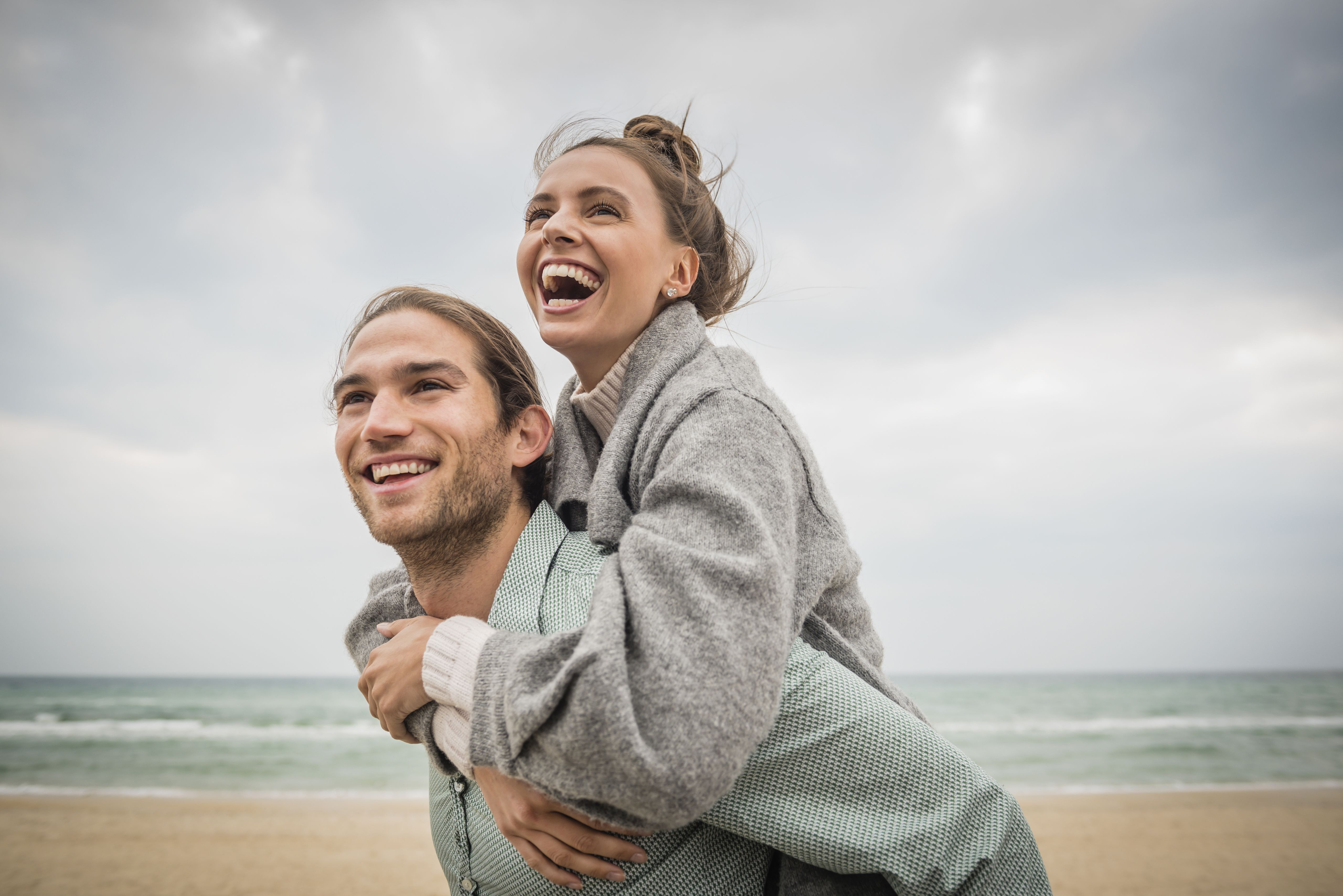 Jeune couple heureux sur une plage ensoleillée, l’homme portant la femme sur son dos, illustrant une rencontre sérieuse, une relation durable et des moments de complicité