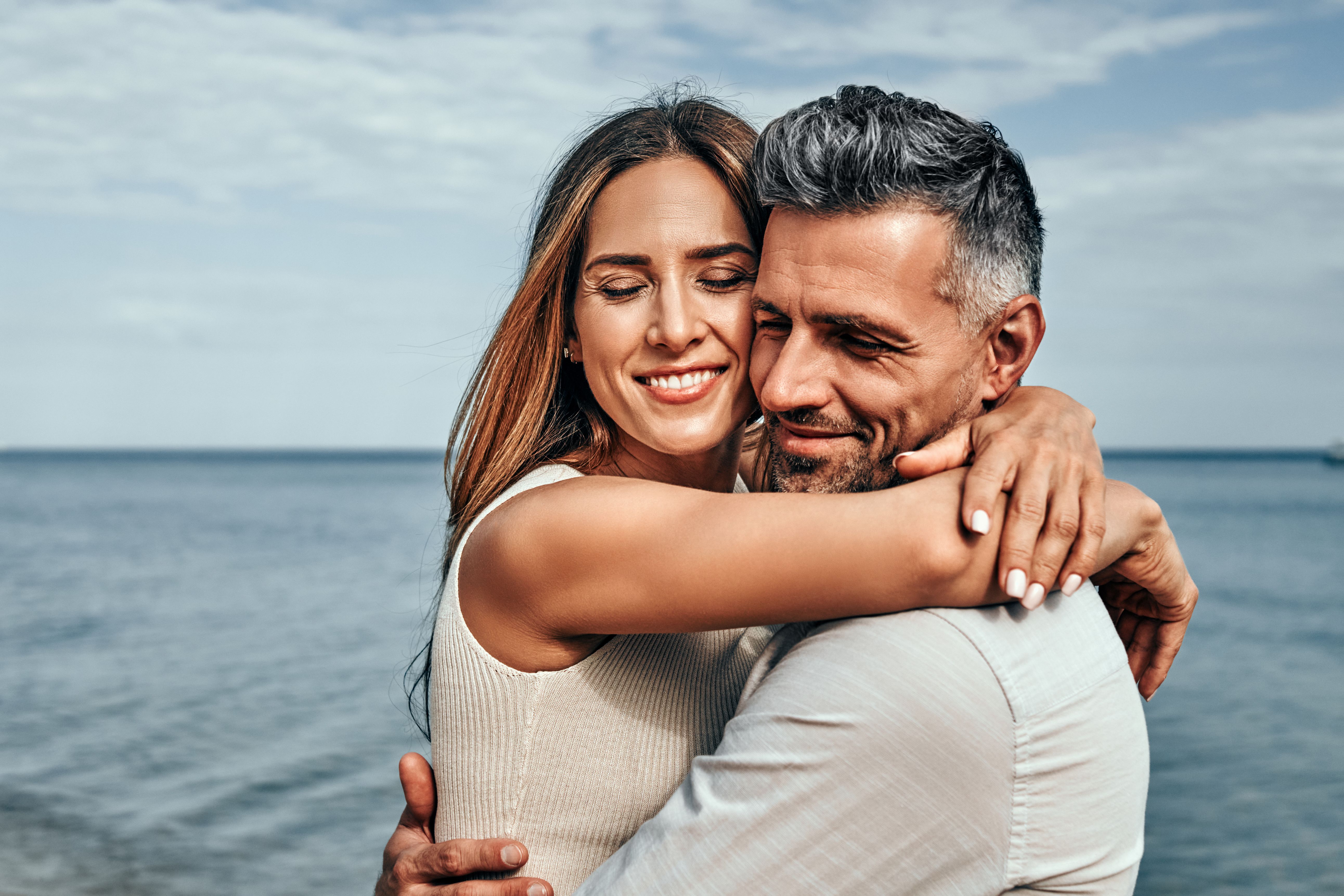 Couple d’une quarantaine d’années s’enlaçant sur une plage en été, illustrant une rencontre sérieuse, une relation durable et la confiance entre partenaires.