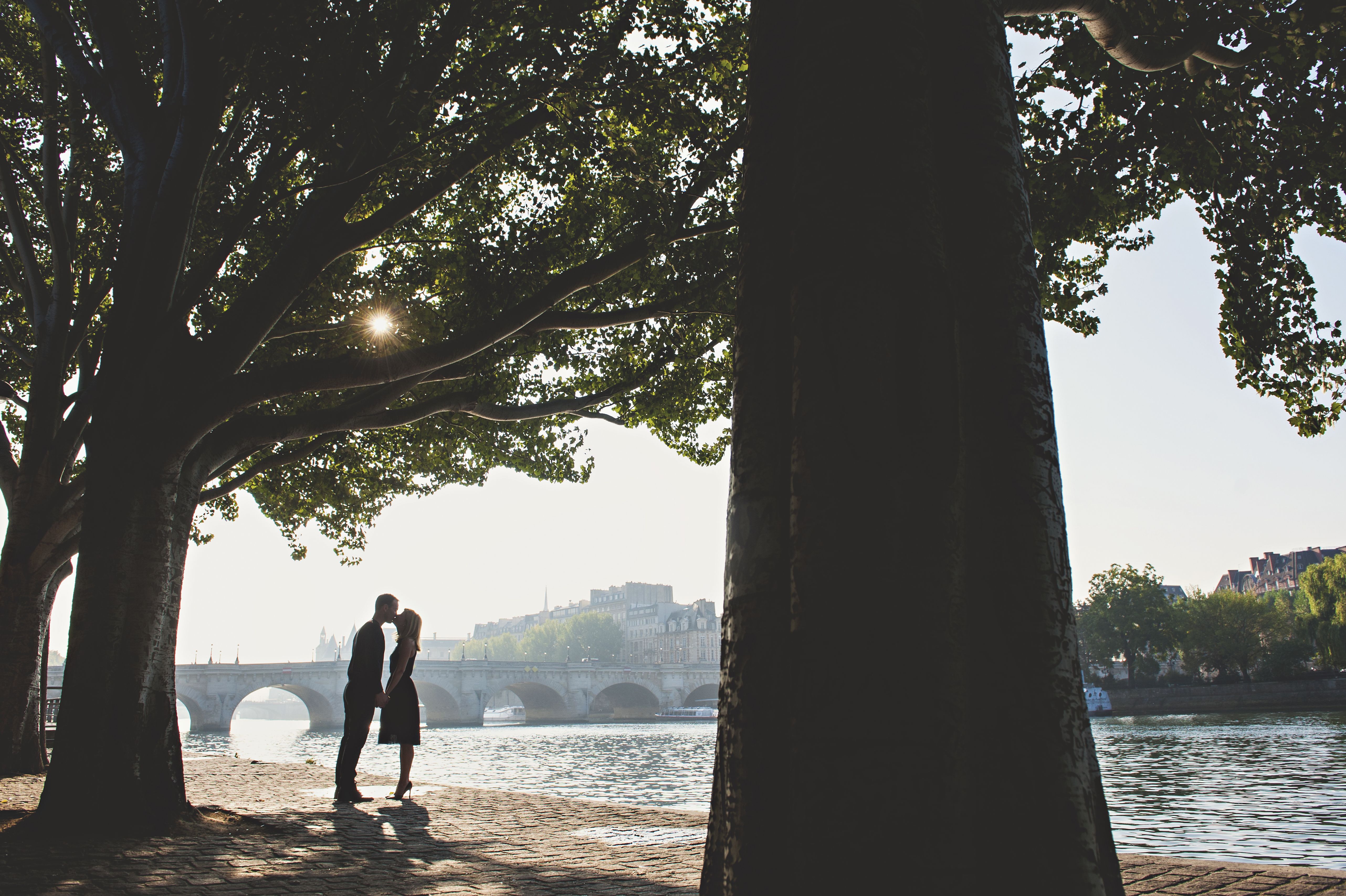 Couple s’embrassant au bord d’un lac devant un ancien pont en pierre, illustrant une rencontre sérieuse, une relation durable et des moments de complicité.