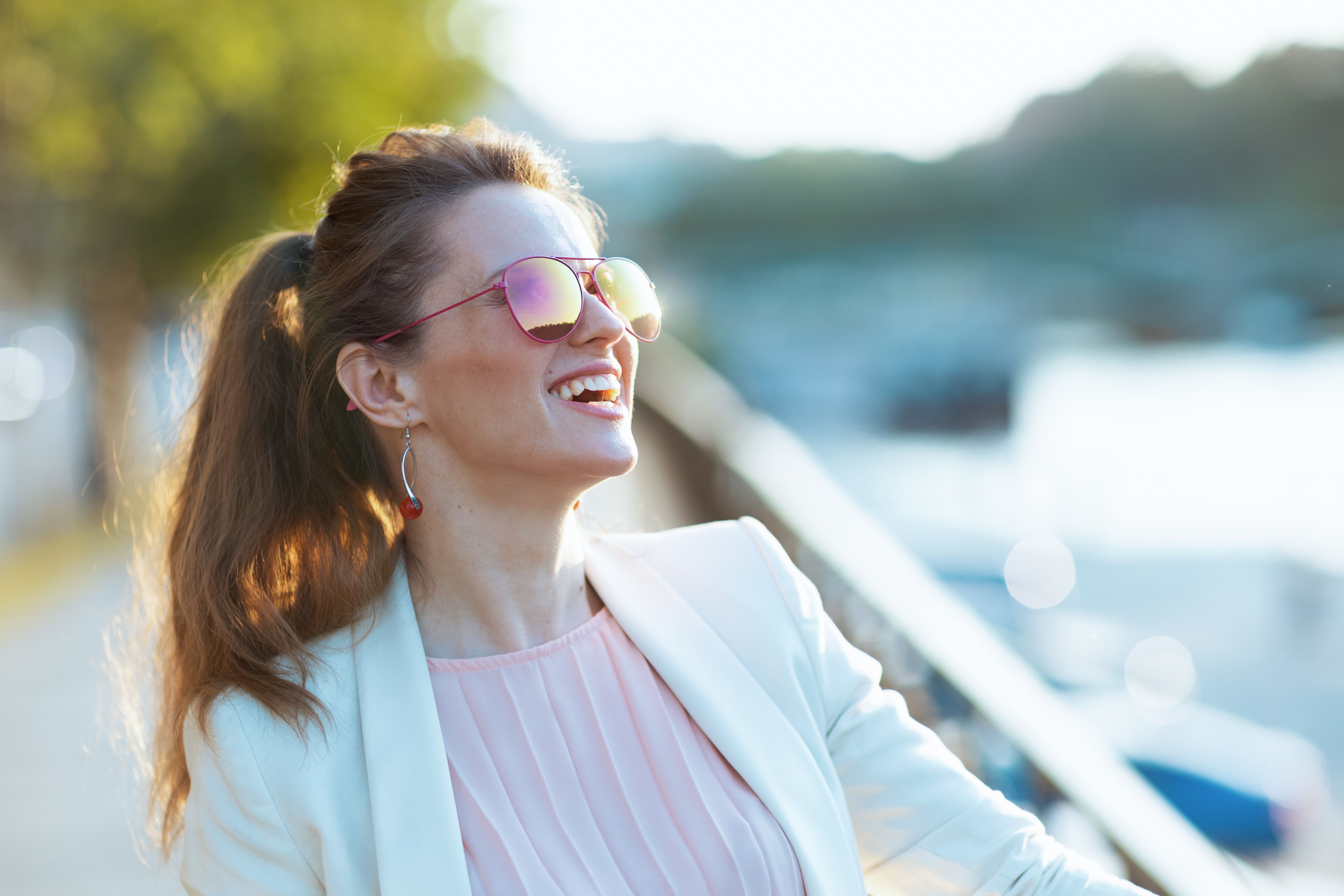 Jeune femme souriante portant des lunettes de soleil, assise à une terrasse en attendant son premier rendez-vous après une rencontre sur un site de rencontre sérieux.